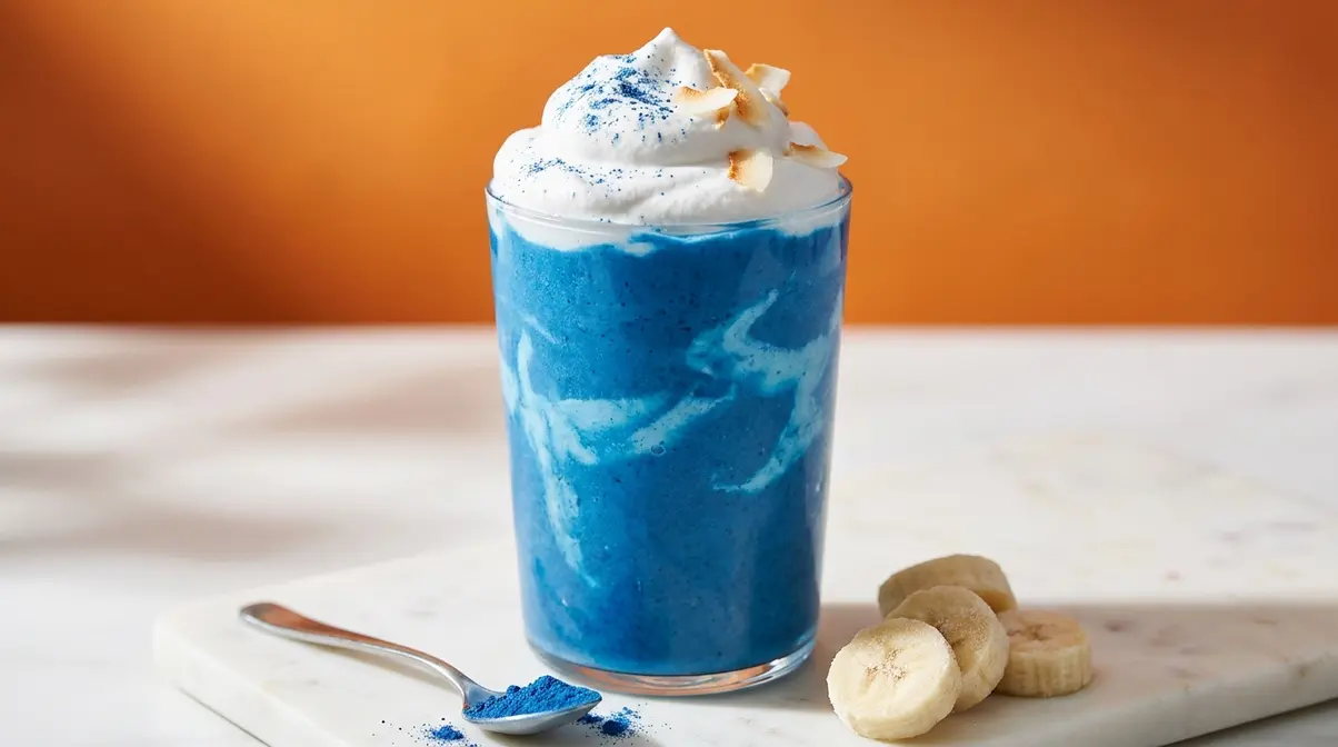 Vibrant blue cloud smoothie made with Blue Majik spirulina in a glass topped with white coconut foam