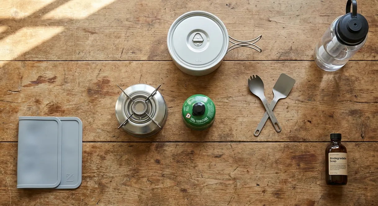 Essential camping gear camp kitchen setup showing stove, pot, and water filter for beginners