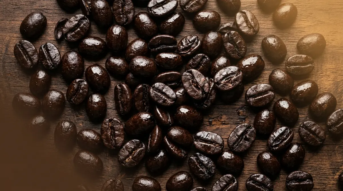 Dark French roast coffee beans with distinctive oily surface sheen on wooden background