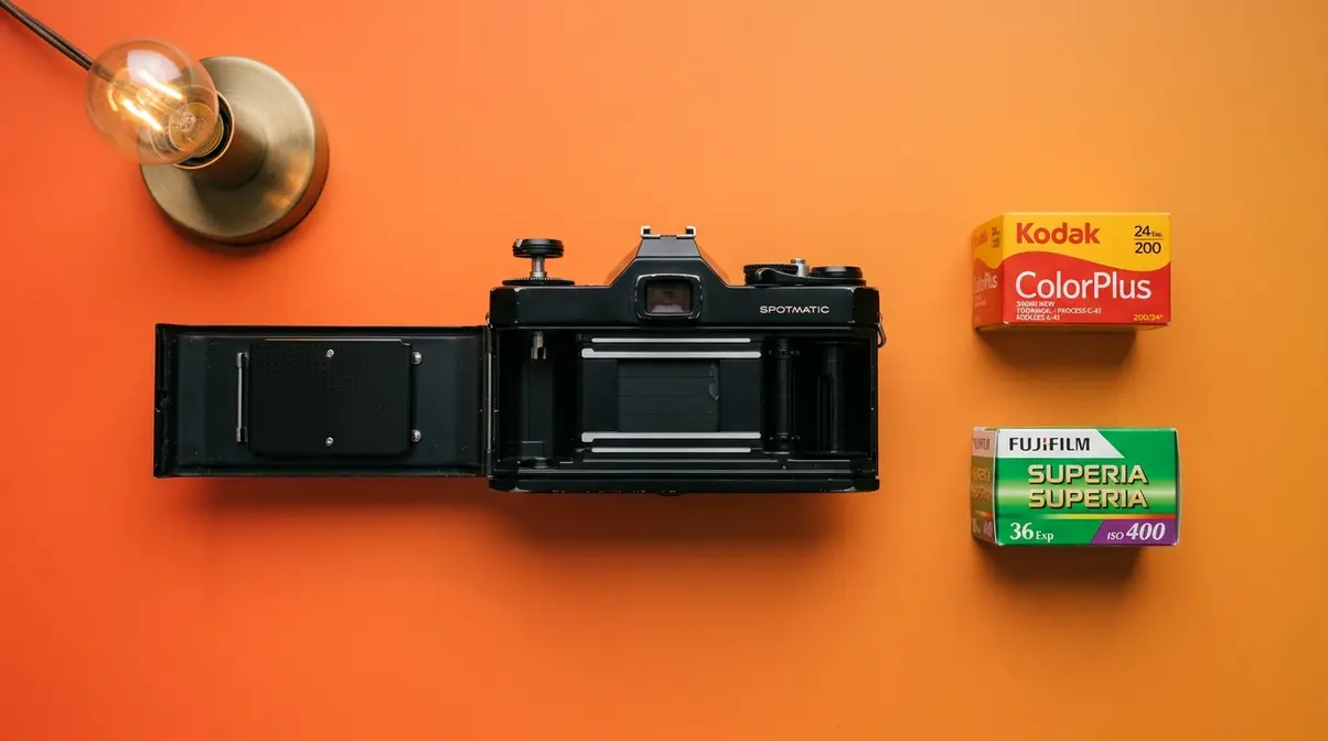 Film photography supplies laid out including camera, fresh film canisters, and shaded workspace