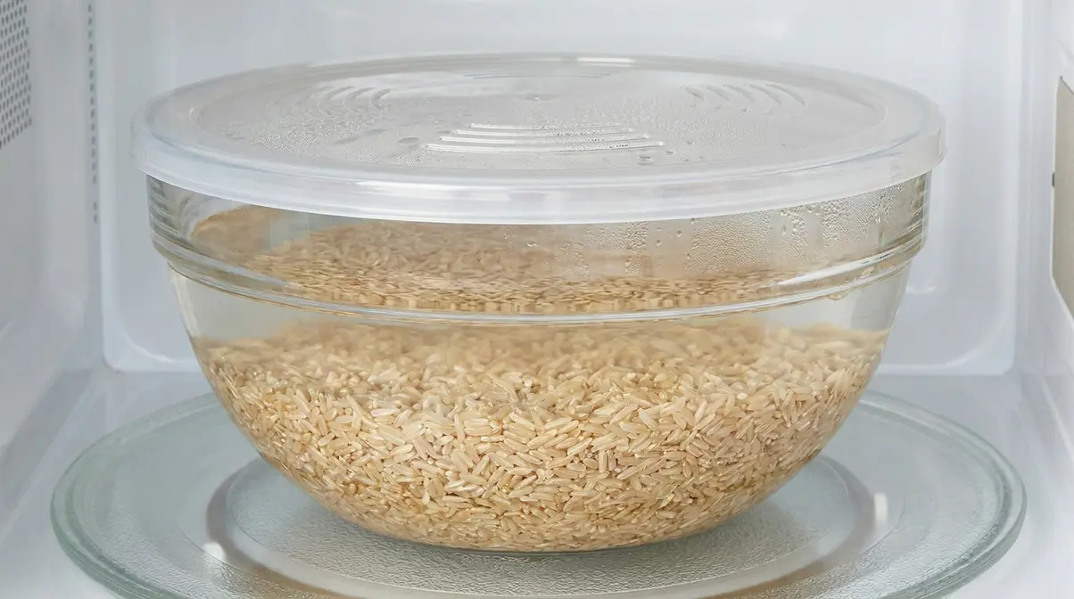 How To Cook Brown Rice Quickly: 4 Fast Methods (2026) 4 Microwave-safe bowl with brown rice and water covered by a vented lid for microwave cooking
