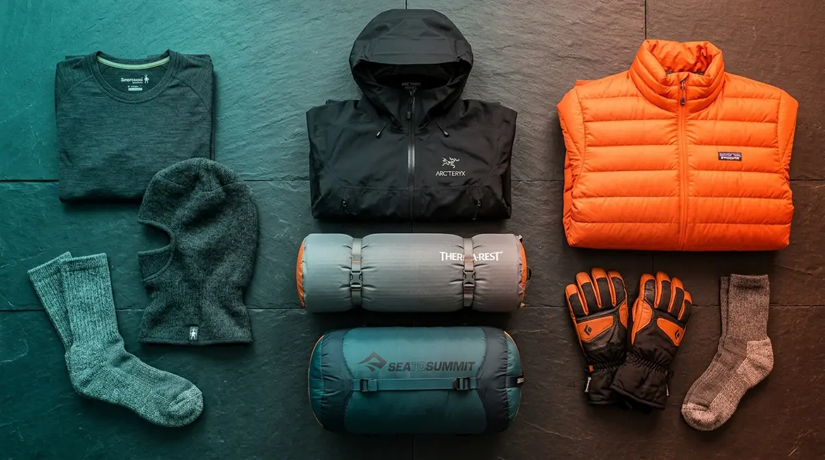 Cold weather camping gear flat lay showing sleeping bag pad base layer down jacket and accessories
