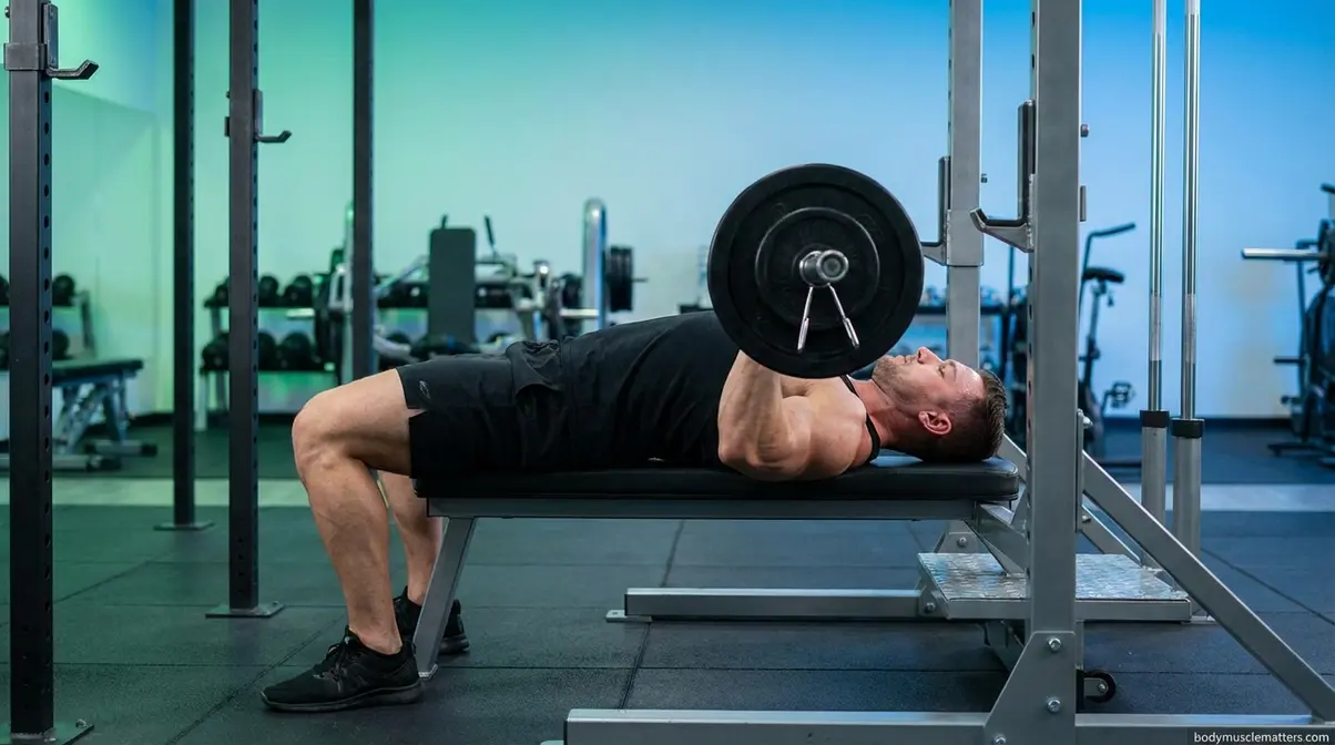Barbell bench press form with safety pins set inside power cage for safe solo training