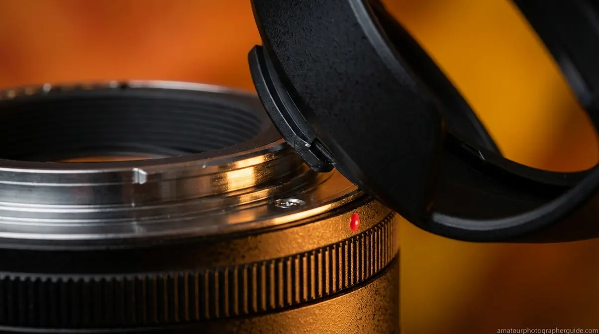 Close-up of camera lens hood bayonet mount connection point showing alignment dot and twist-lock ridges
